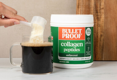 Hand pouring a scoop of Bulletproof Unflavored Collagen Protein into a clear mug full of coffee.