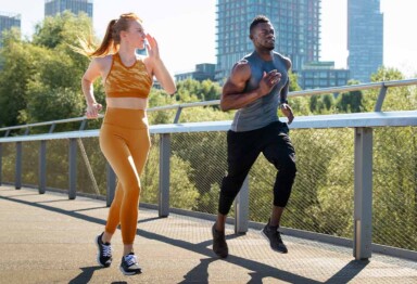 Couple in athletic apparel running along a sidewalk with a cityscape in the background.