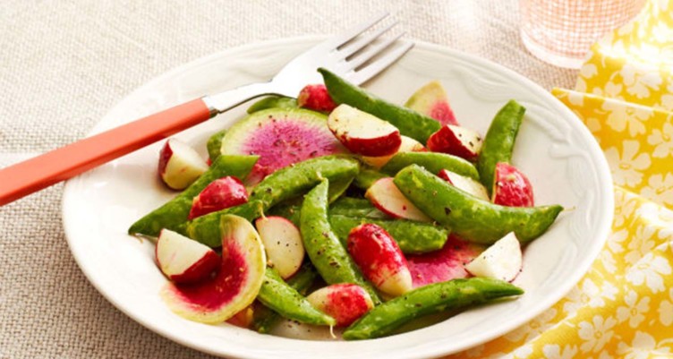 Sugar snap peas and radishes on white plate with fork