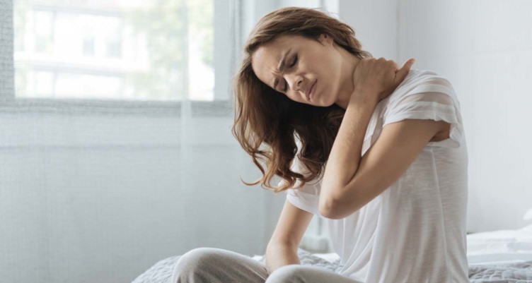 Woman rubbing neck while sitting on bed