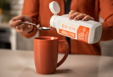 Woman in orange jacket pouring Brain Octane Oil onto a spoon above orange mug