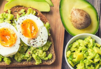 Seasoned avocado toast with a hard boiled egg cut in half laying atop a cutting board