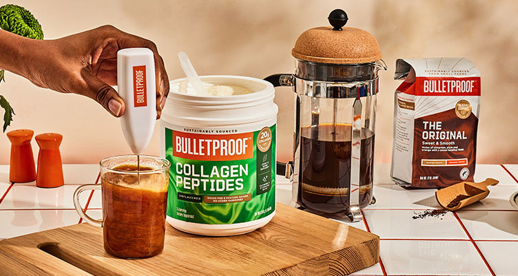 hand holds a coffee frother mixing together unflavored collagen peptides into a cup of coffee next to a french press and a bag of original coffee