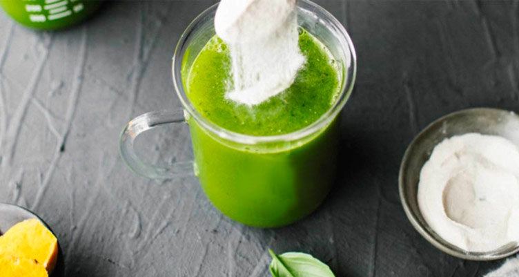 a scoop of unflavored collagen peptides falls into a clear glass of green juice