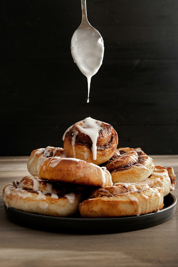 Plate full of paleo cinnamon rolls stacked upon one another with a spoon drizzling icing