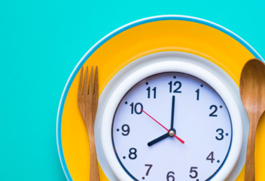 Clock on yellow plate next to wooden utensils