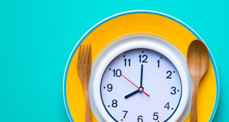 Clock on yellow plate next to wooden utensils