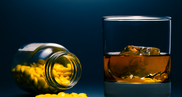 Bottle of pills next to glass of alcohol