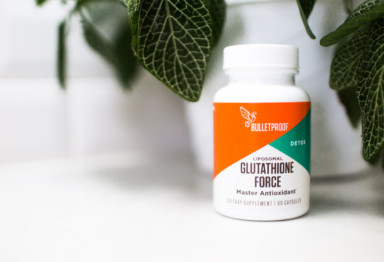 Dark leaves and bottle of Bulletproof Glutathione Force on white countertop