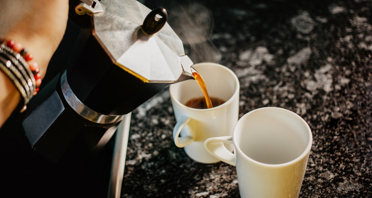 Person pouring coffee from moka pot into mug