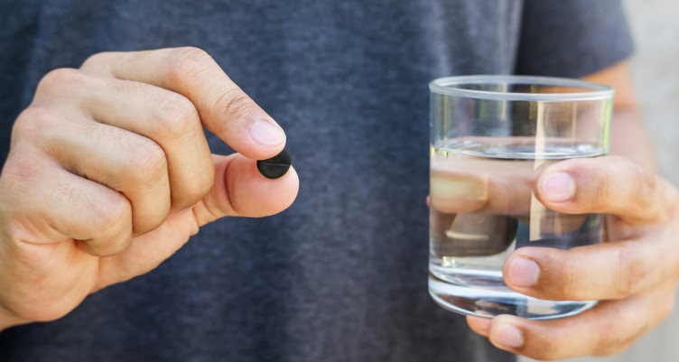 Person holding charcoal pill and glass of water
