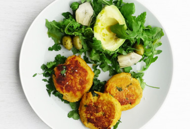 Three salmon patties on white plate with greens and avocado