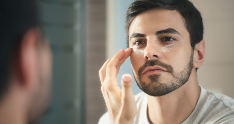 man applying skin products in mirror