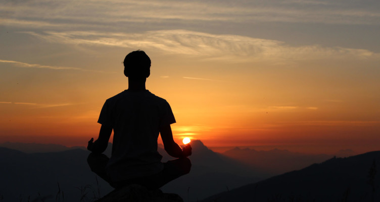 A person meditating at sunset