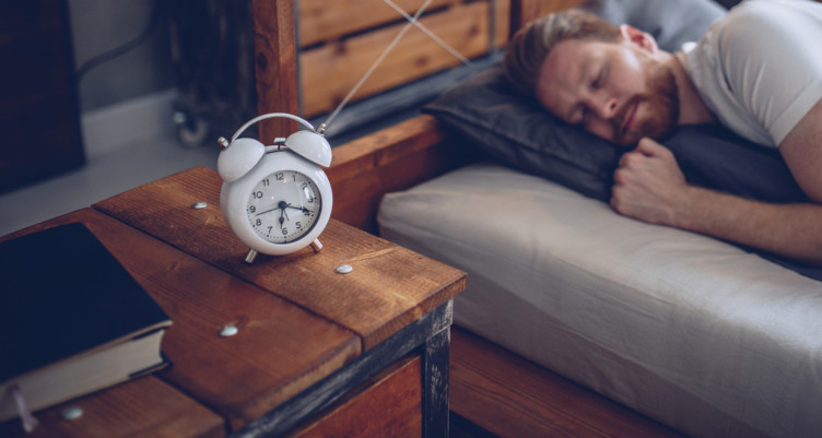 Person sleeping in bed next to white alarm clock