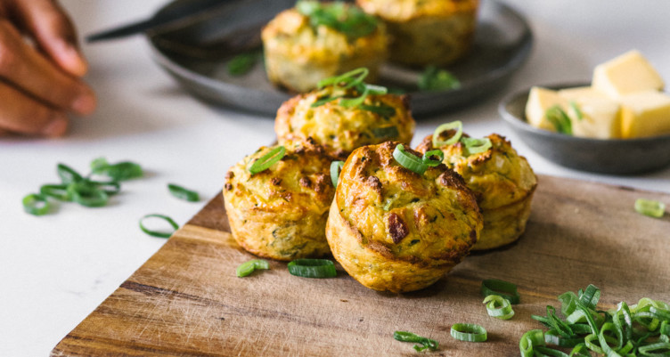 a cutting board with freshly baked muffins topped with greens