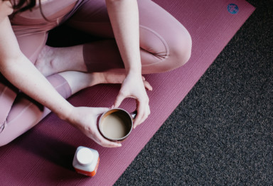 Woman holding full coffee mug on yoga mat