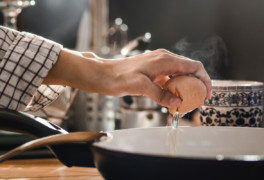 person cracking egg into skillet for breakfast