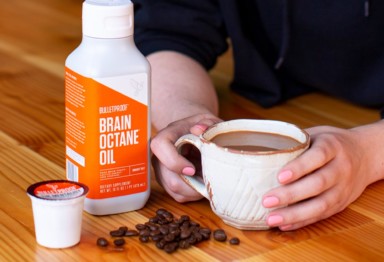 Woman holding a cup of Bulletproof coffee next to a bottle of Brain Octane Oil an MCT oil product