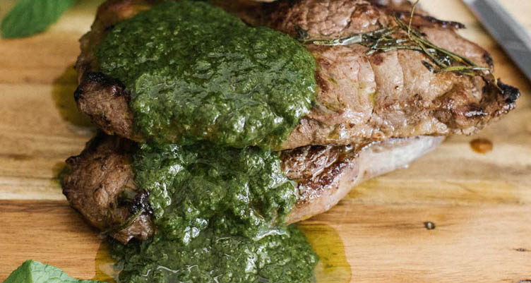 Steak with green chimichurri sauce on wooden board
