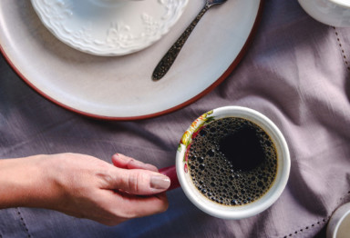 Person holding cup of coffee next to plate