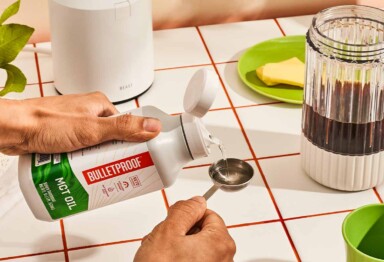 Hands measuring MCT oil next to a blending with coffee inside