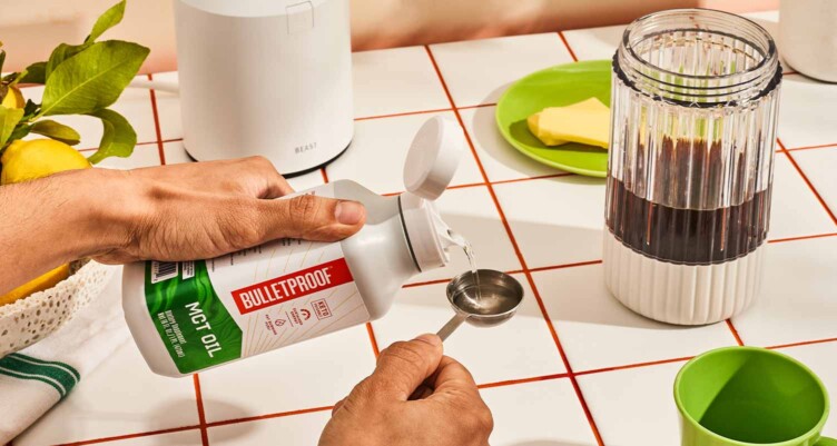 Hands measuring MCT oil next to a blending with coffee inside