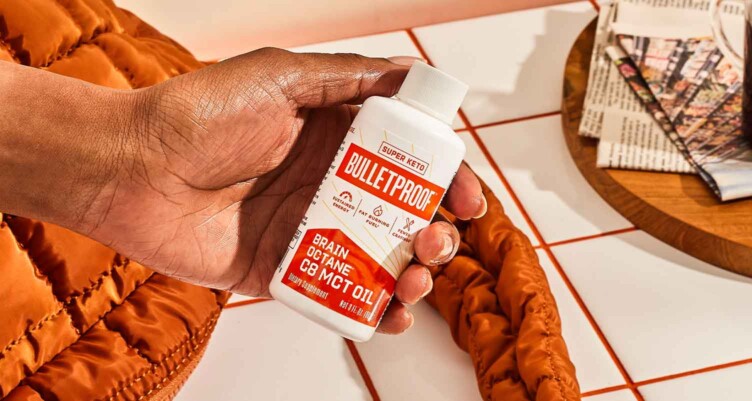 Hand holding a 3oz bottle of Brain Octane Oil with orange plush bag in the background