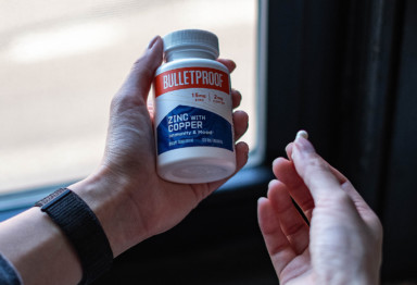 A person holding a bottle of Bulletproof Zinc With Copper with one pill in the other hand.