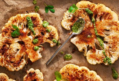 Roasted cauliflower with chimichurri sauce drizzling on parchment paper.
