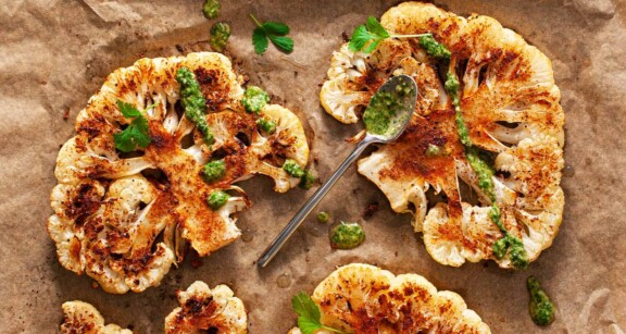 Roasted cauliflower with chimichurri sauce drizzling on parchment paper.