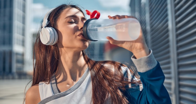 A woman with headphones drinking from a water bottle