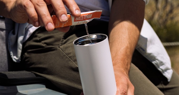A hand pouring a Bulletproof Brain Octane Oil Go Packet into a coffee mug