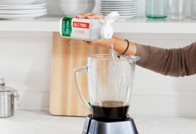 A person pouring Bulletproof MCT Oil into a blender filled with coffee
