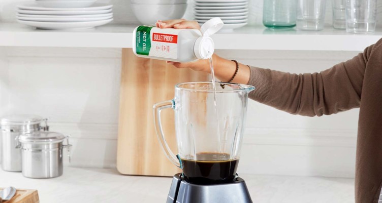 A person pouring Bulletproof MCT Oil into a blender filled with coffee