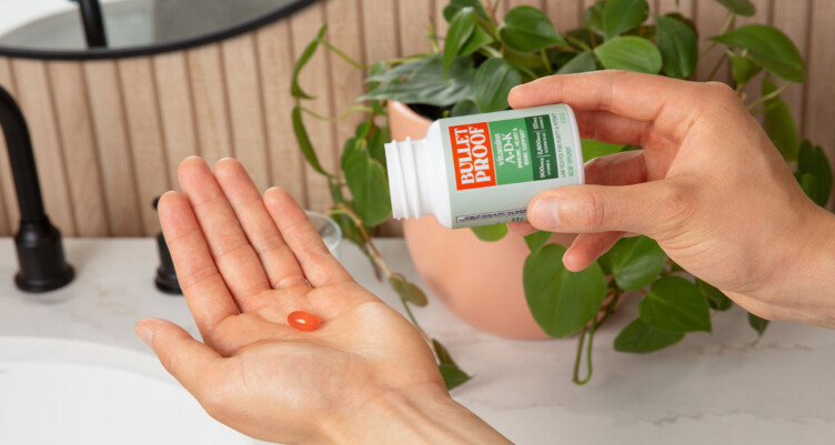 Hand pouring a bottle of Bulletproof Vitamin A-D-K supplement into another hand in a bathroom setting.