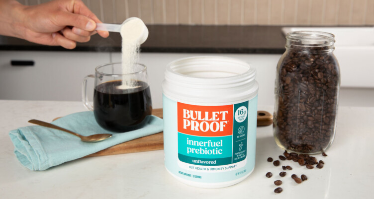 Hand scooping Bulletproof Innerfuel Prebiotics in a coffee mug in a kitchen setting with a mason jar of coffee beans nearby.