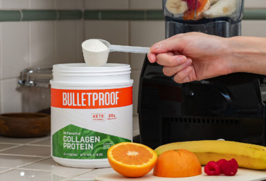 A hand scooping Bulletproof Unflavored Collagen Protein from a tub next to fresh fruit