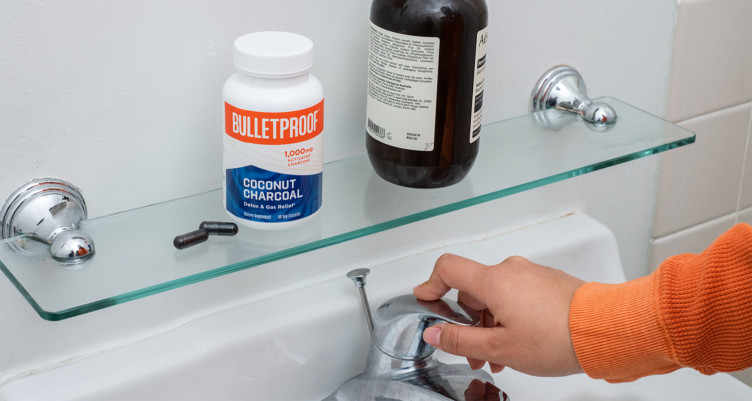 Two Bulletproof Coconut Charcoal capsules and accompanying bottle on shelf above a bathroom sink