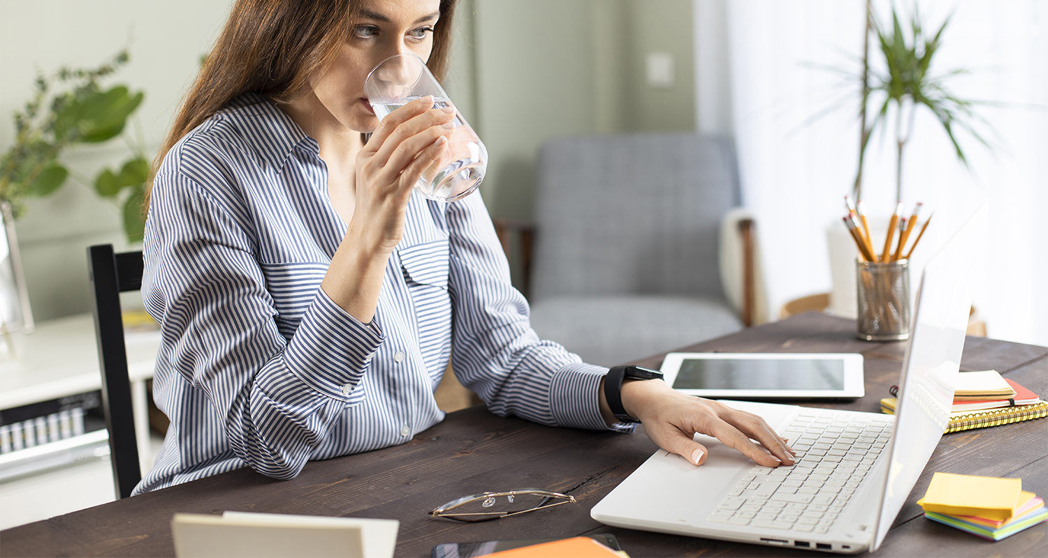 A woman drinking a glass of water at her desk
