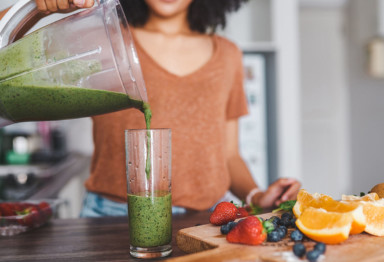 A woman pouring a green smoothie from a blender into a glass