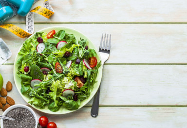 Plate of salad, tape measure, water bottle and weights to promote weight management