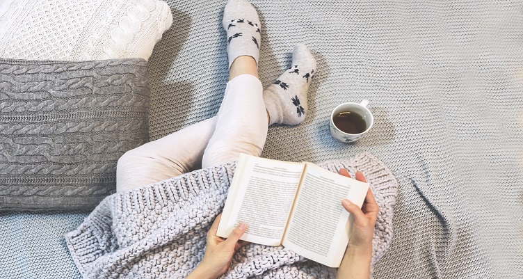 A person reading a book with tea in bed
