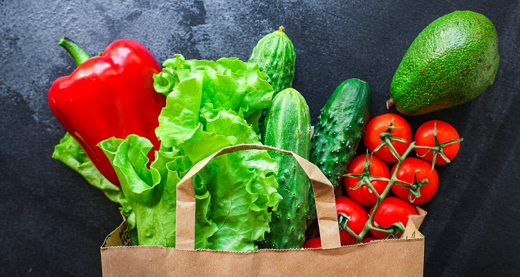 A grocery bag filled with green and red produce