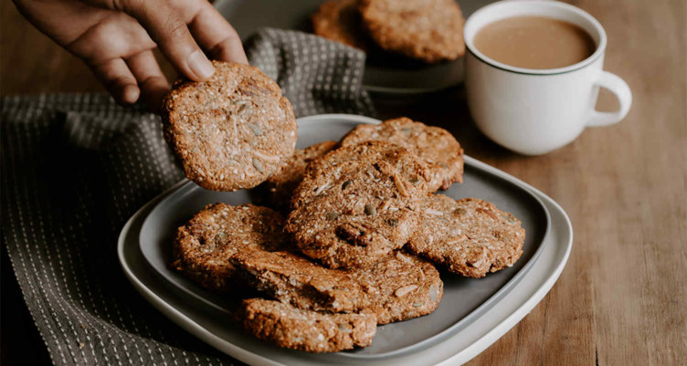 hand picking up a cookie from a plate of cookies next to a cup of hot coffee