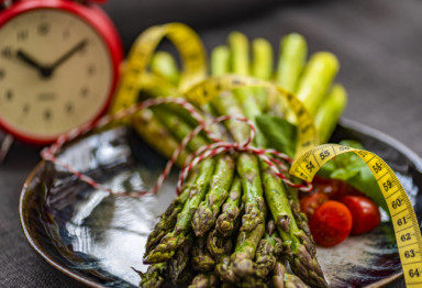 A tied bundle of asparagus next to a clock