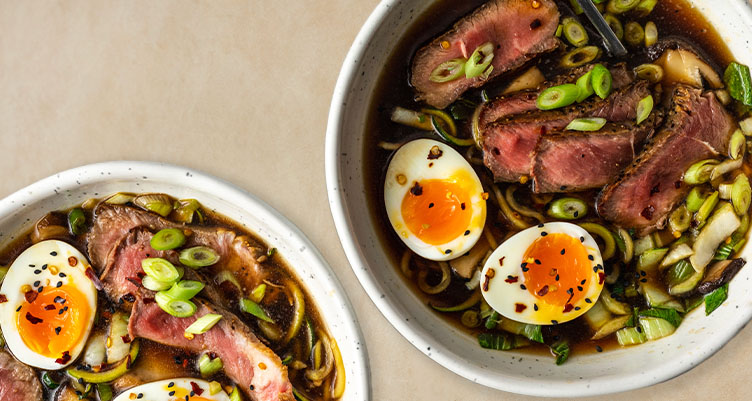 2 bowls of ramen with eggs and beef sits on table