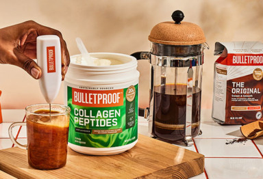 hand holds coffee frother in cup frothing coffee next to a container of bulletproof unflavored collagen peptides, a french press, and original coffee grounds