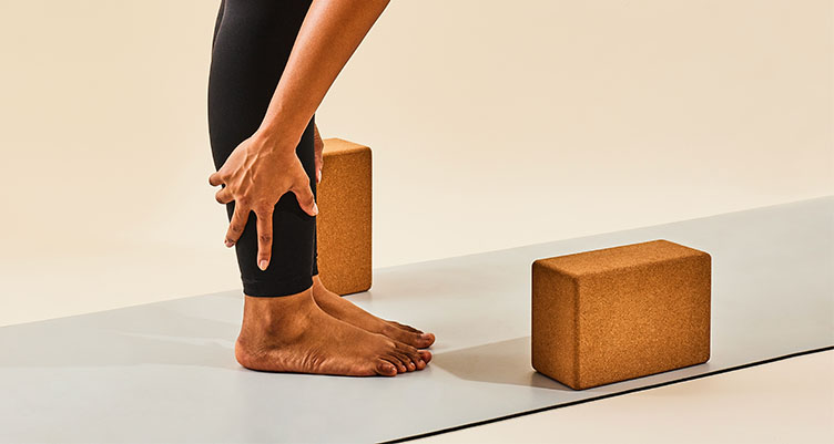 woman in black leggings stretching on yoga mat with yoga block