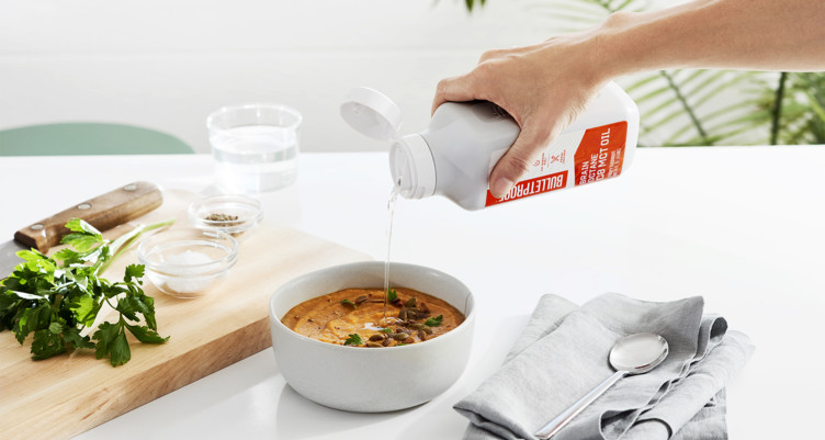 A person pouring Brain Octane Oil into a bowl of soup